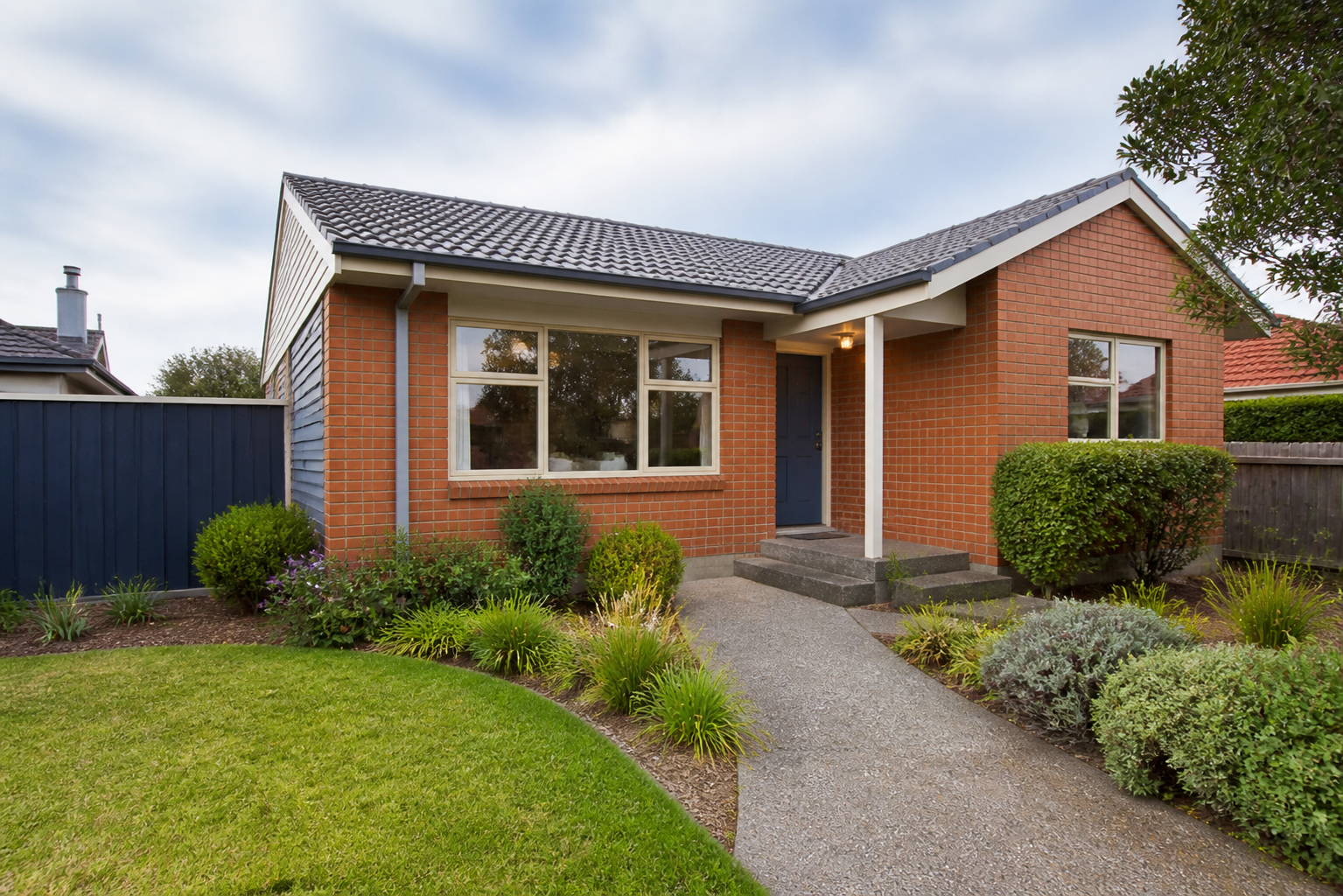 A neat single-storey brick rental home with a clear path, maintained garden and blue front door.